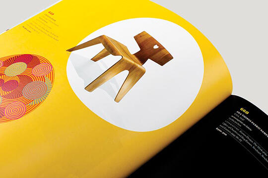 Open magazine with a wooden chair on a white circle set against a bright yellow background. To the left, colorful circular patterns.