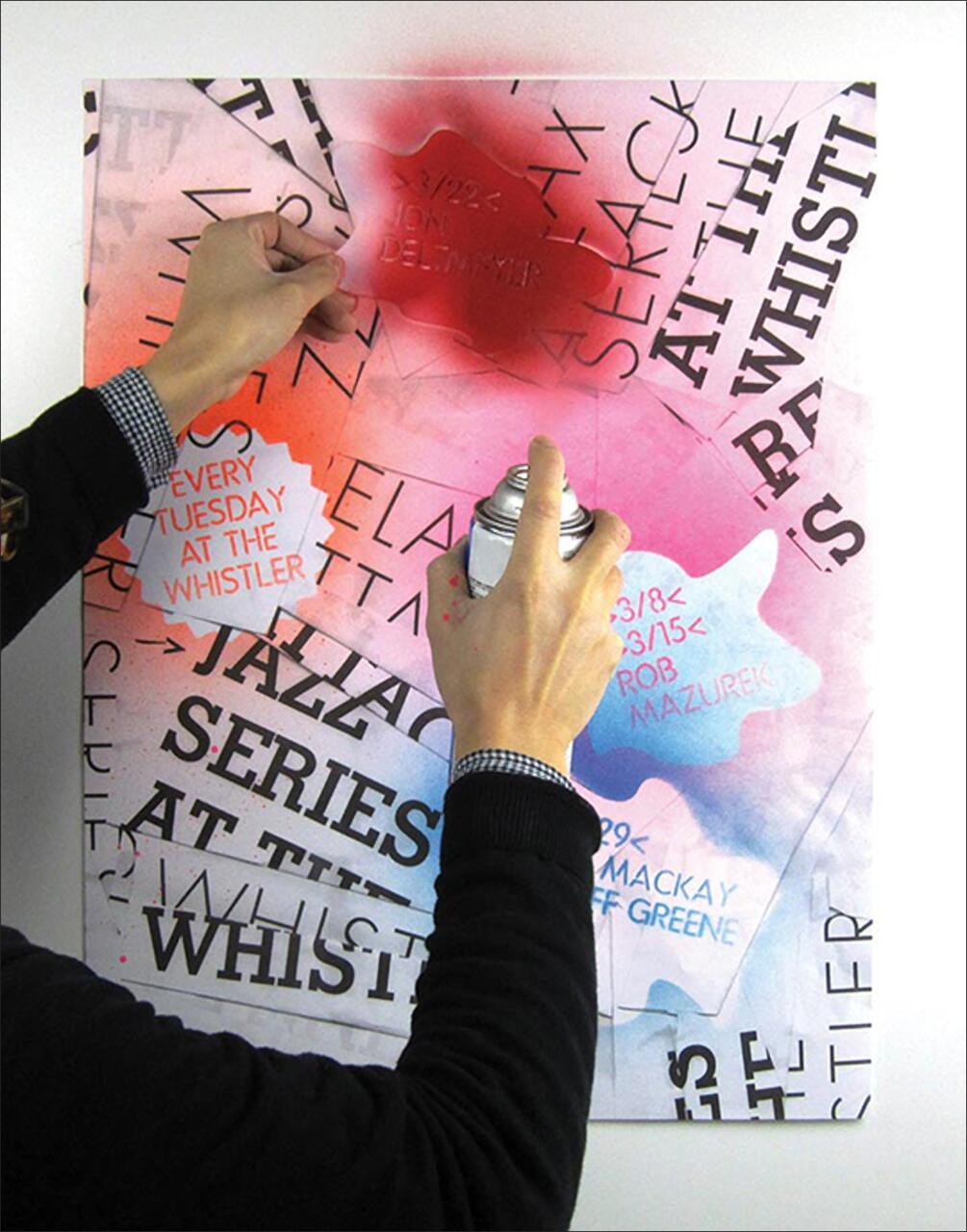 Hands spray painting text onto a colorful poster with overlapping bold and cursive words in red, black, and blue on a white background.