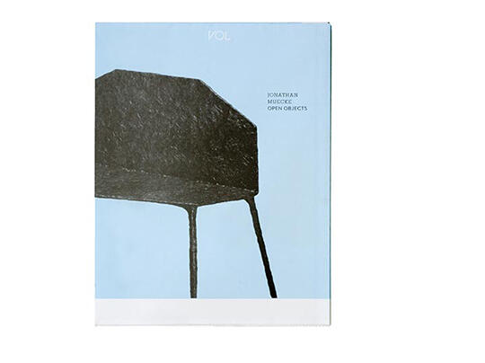 A minimalist book cover with a large, abstract black chair on a pale blue background. Text in the upper right corner reads "Jonathan Muecke Open Objects" with "VOL" at the top.