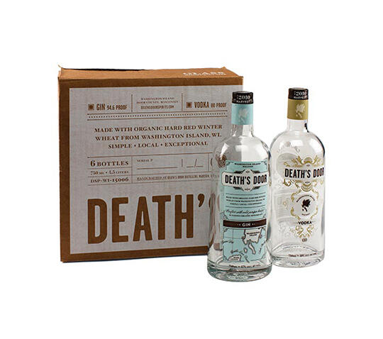 Two bottles of Death's Door spirits, one gin and one vodka, stand in front of a brown cardboard box with branding. The gin bottle features a blue map design, while the vodka bottle has a clear, elegant label. The box lists product details.