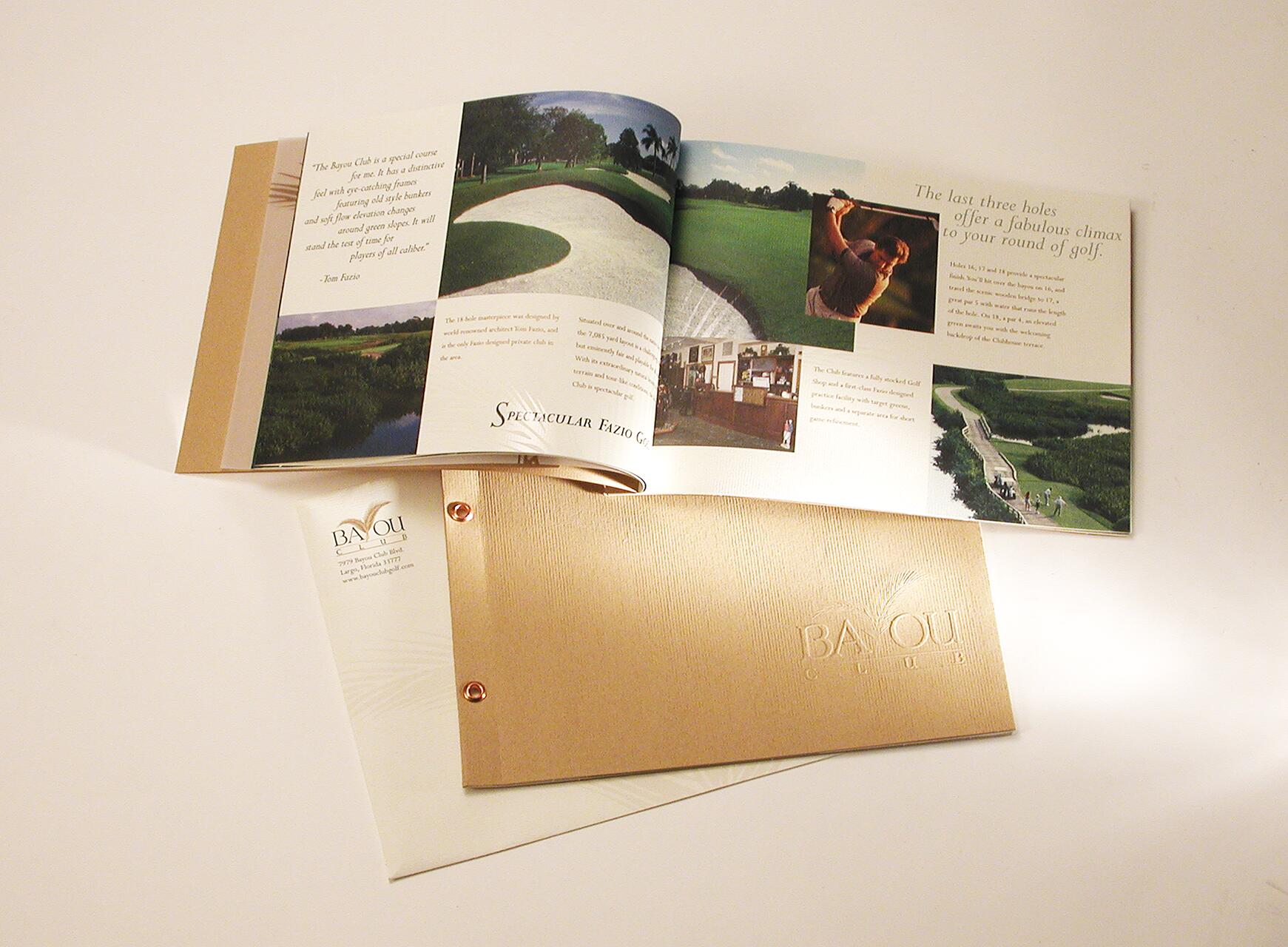 Open brochure showcasing a golf course with photos of a course, a golfer swinging, and clubhouse interiors. Text describes the course's appeal. A closed, embossed cover with "Bayou Club" sits underneath.