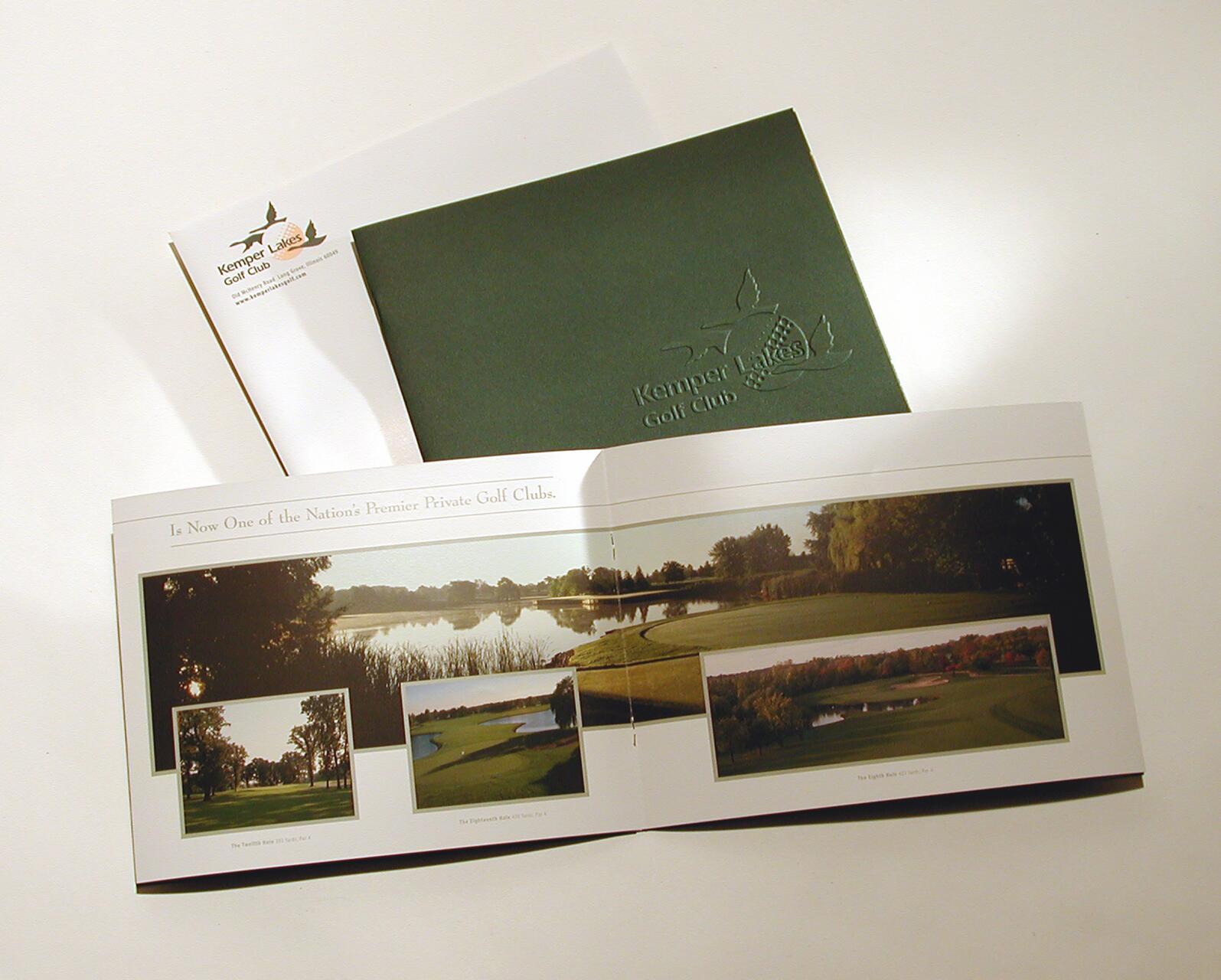 Brochure showcasing a golf course with images of green fields and water hazards. A green folder embossed with "Kemper Lakes Golf Club" is partially visible behind it.