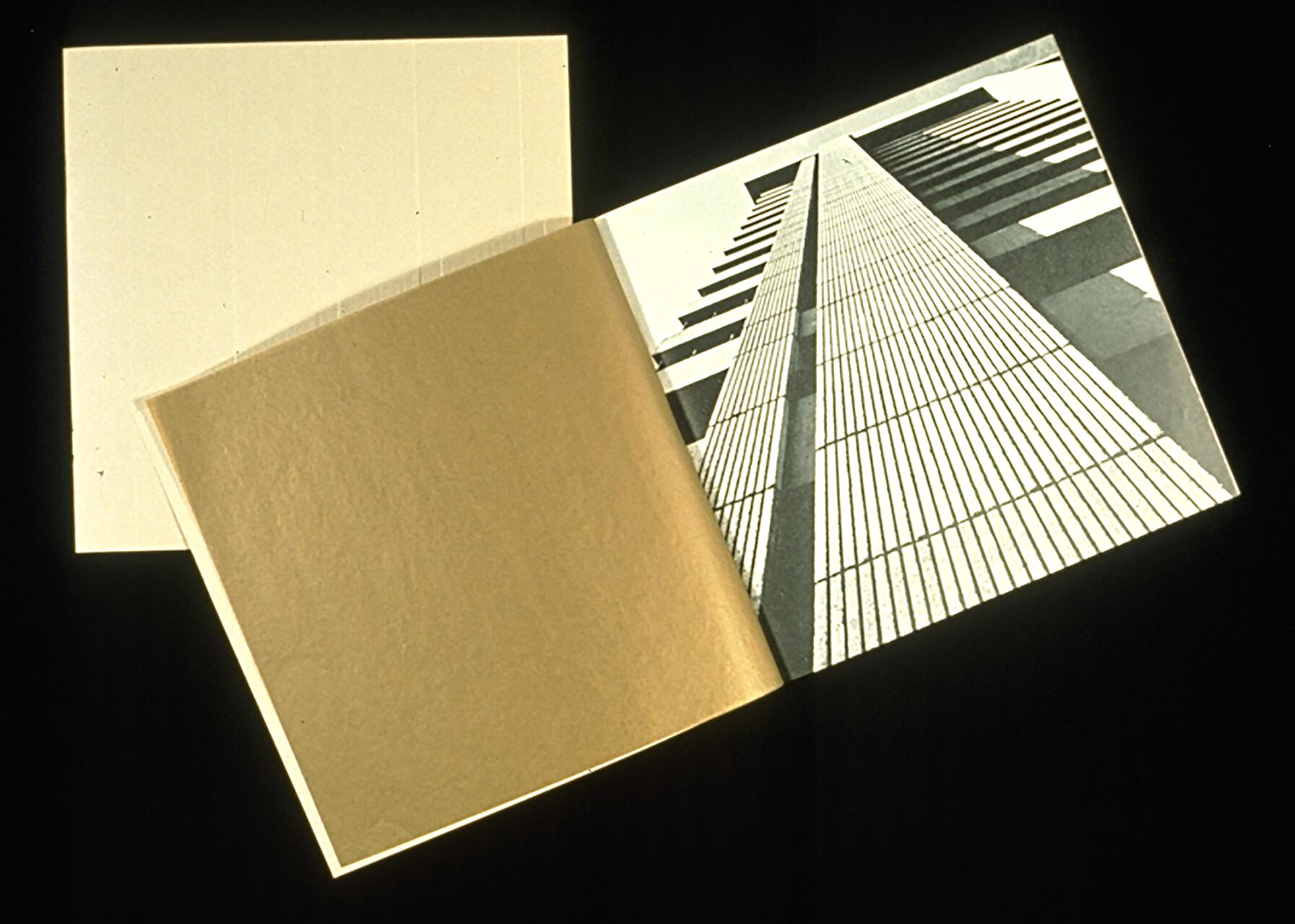 Open book with a sepia-toned page on the left and a black-and-white photograph of a tall building from a low angle on the right, against a black background.