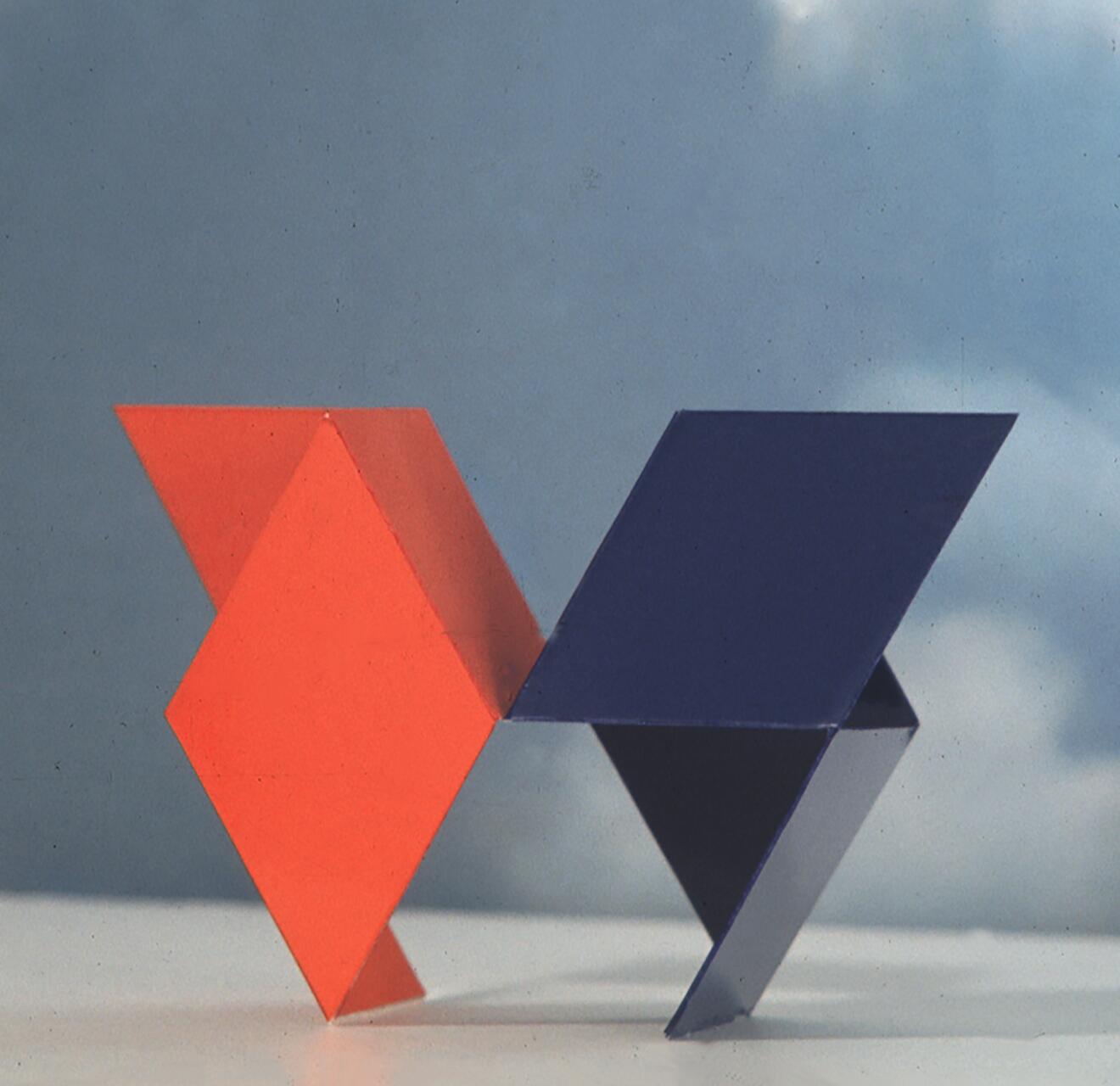 Red and blue geometric shapes resembling arrows, standing upright against a cloudy sky background.