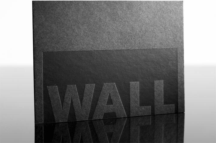 Black card with the word "WALL" embossed in large capital letters, set on a reflective surface.