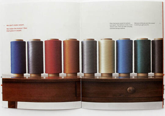 Spools of thread in various colors including gray, red, orange, brown, cream, blue, and teal are neatly lined up on a wooden surface, suggesting a focus on textiles or materials.