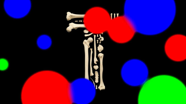 Skeleton arranged in the shape of the letter 'T' against a black background, surrounded by large, colorful, blurred circles in red, blue, and green.