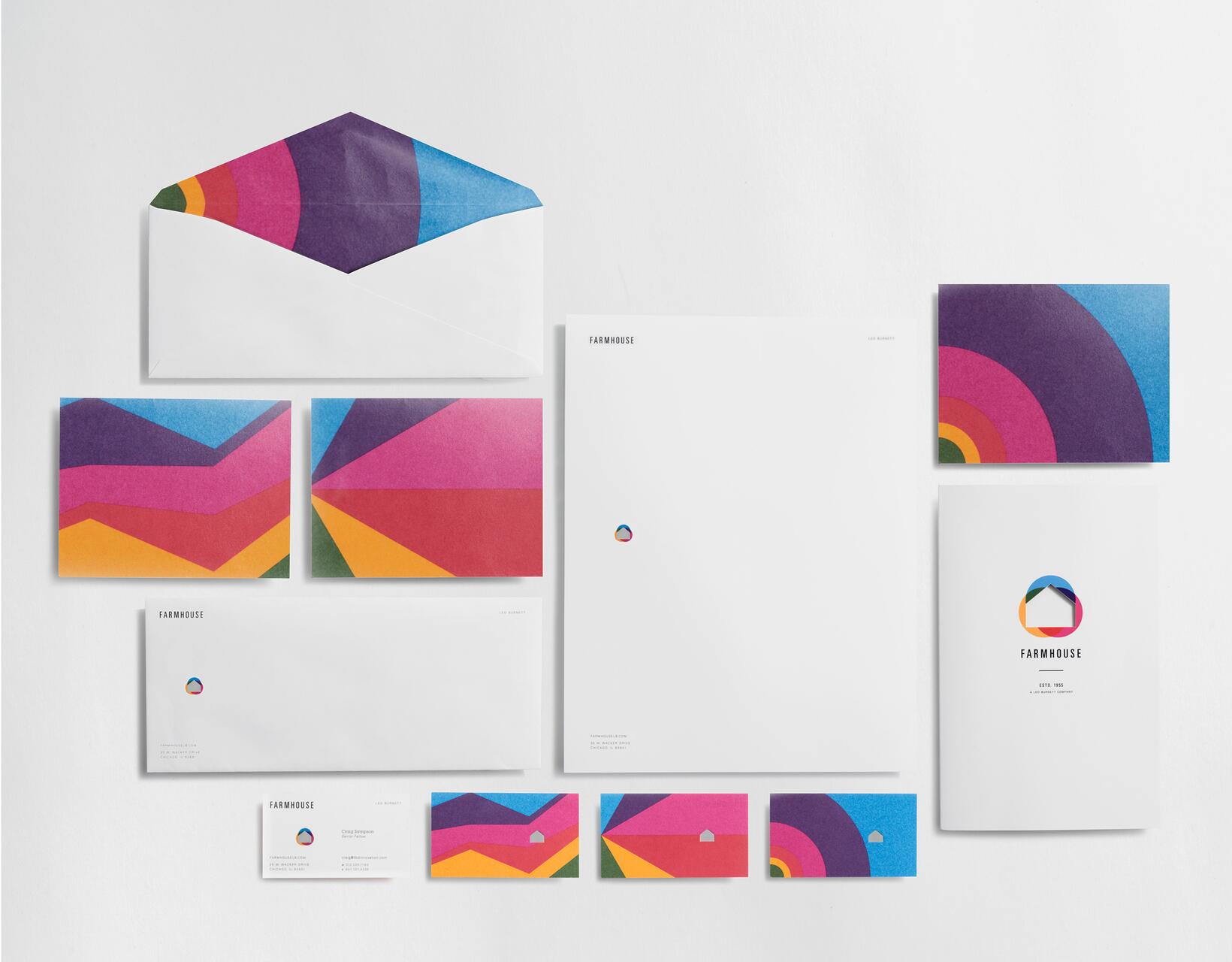 Colorful stationery set with envelopes, business cards, letterhead, and a booklet featuring a vibrant geometric design in purple, pink, orange, and blue.
