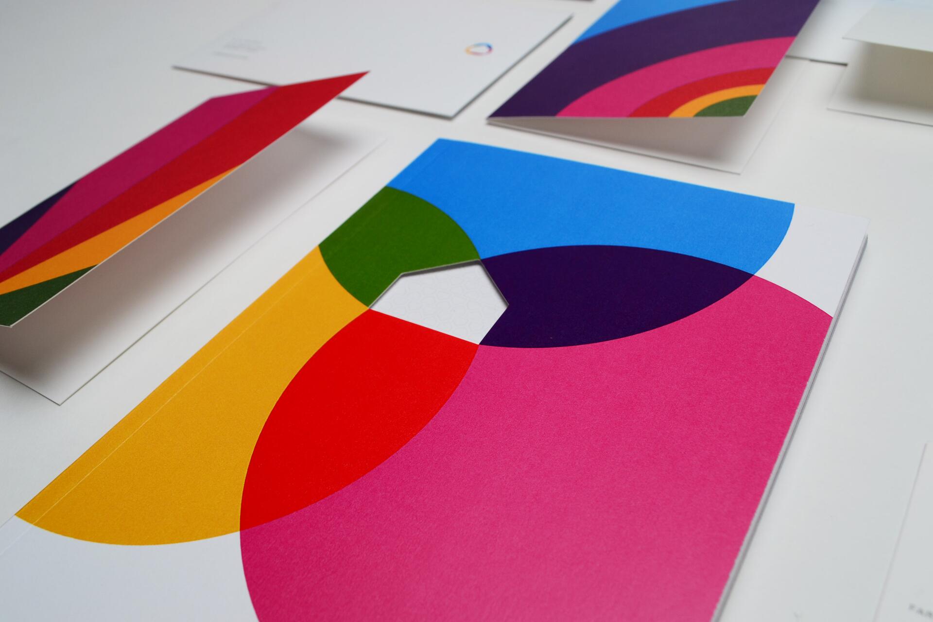 Colorful geometric patterns on white paper, featuring overlapping circles in blue, pink, red, yellow, green, and purple. Some sheets are folded and arranged on a flat surface.