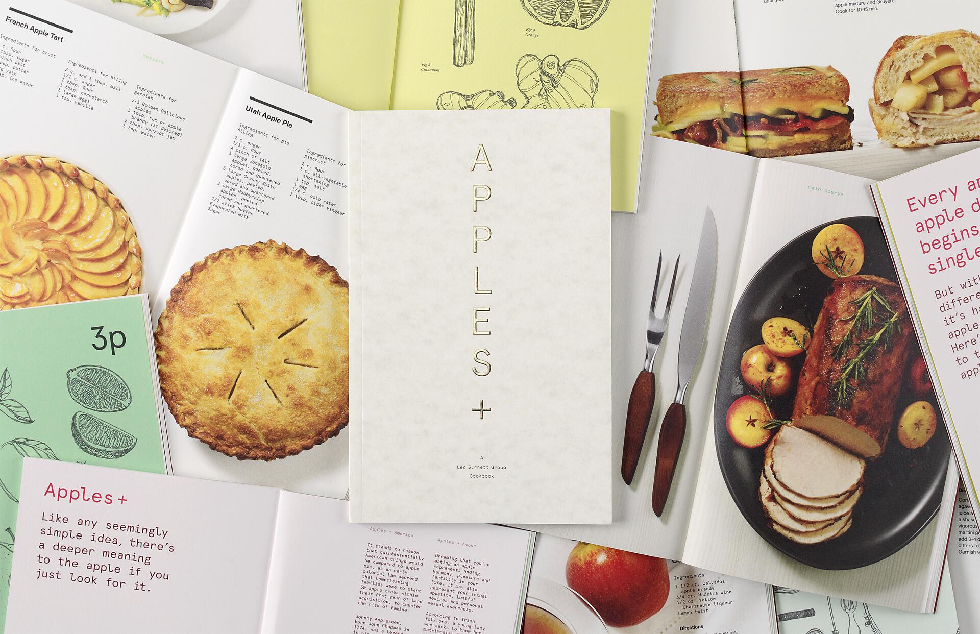 Cookbook cover titled "APPLES+" surrounded by open pages with apple recipes, including a pie, a tart, and a meat dish. Various illustrations and dishes highlight apple-themed cuisine.