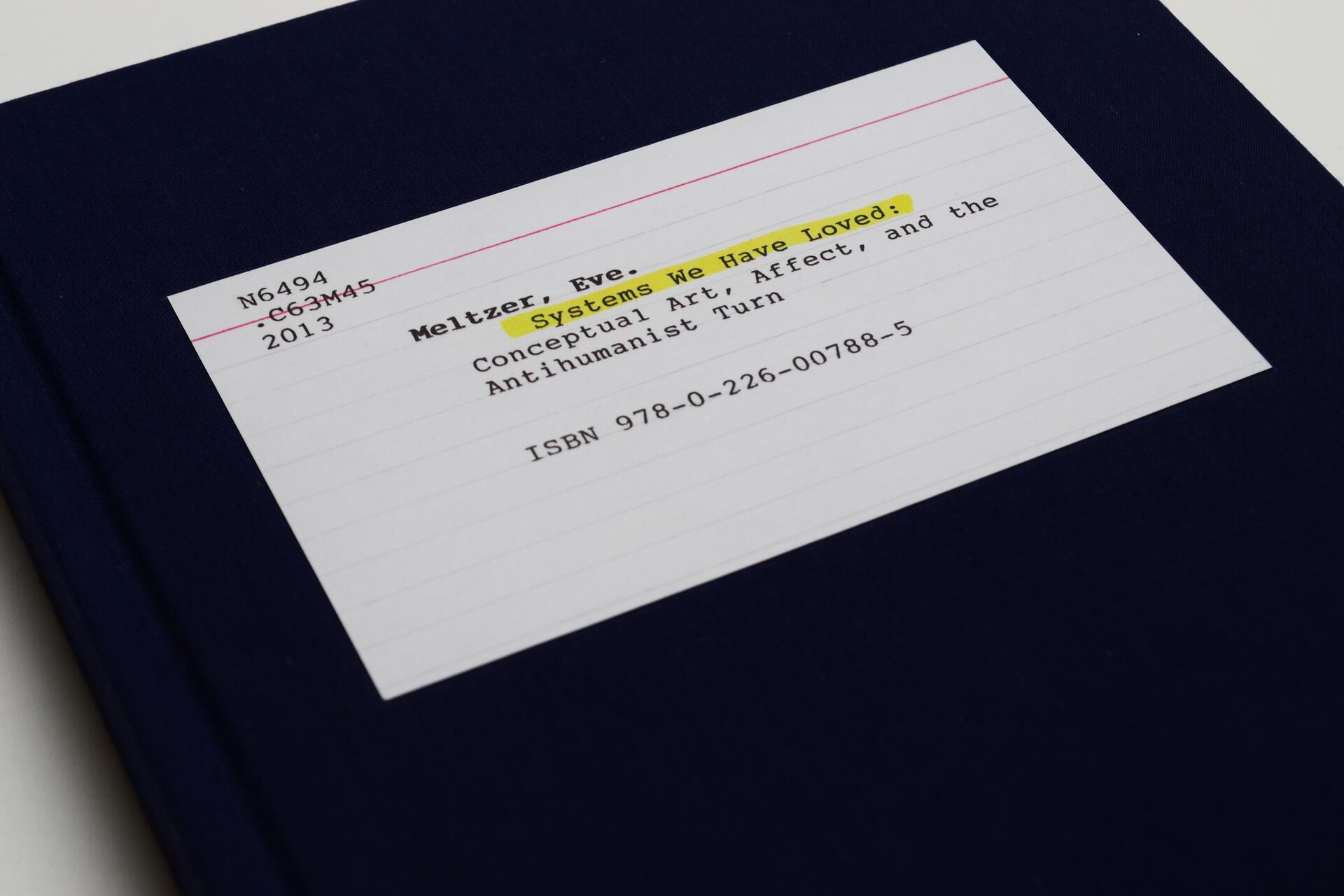 Book cover featuring a white label on a dark blue background, with highlighted text "Systems We Have Loved" by Meltzer, Eve. The label includes a library call number, publication year 2013, and ISBN.