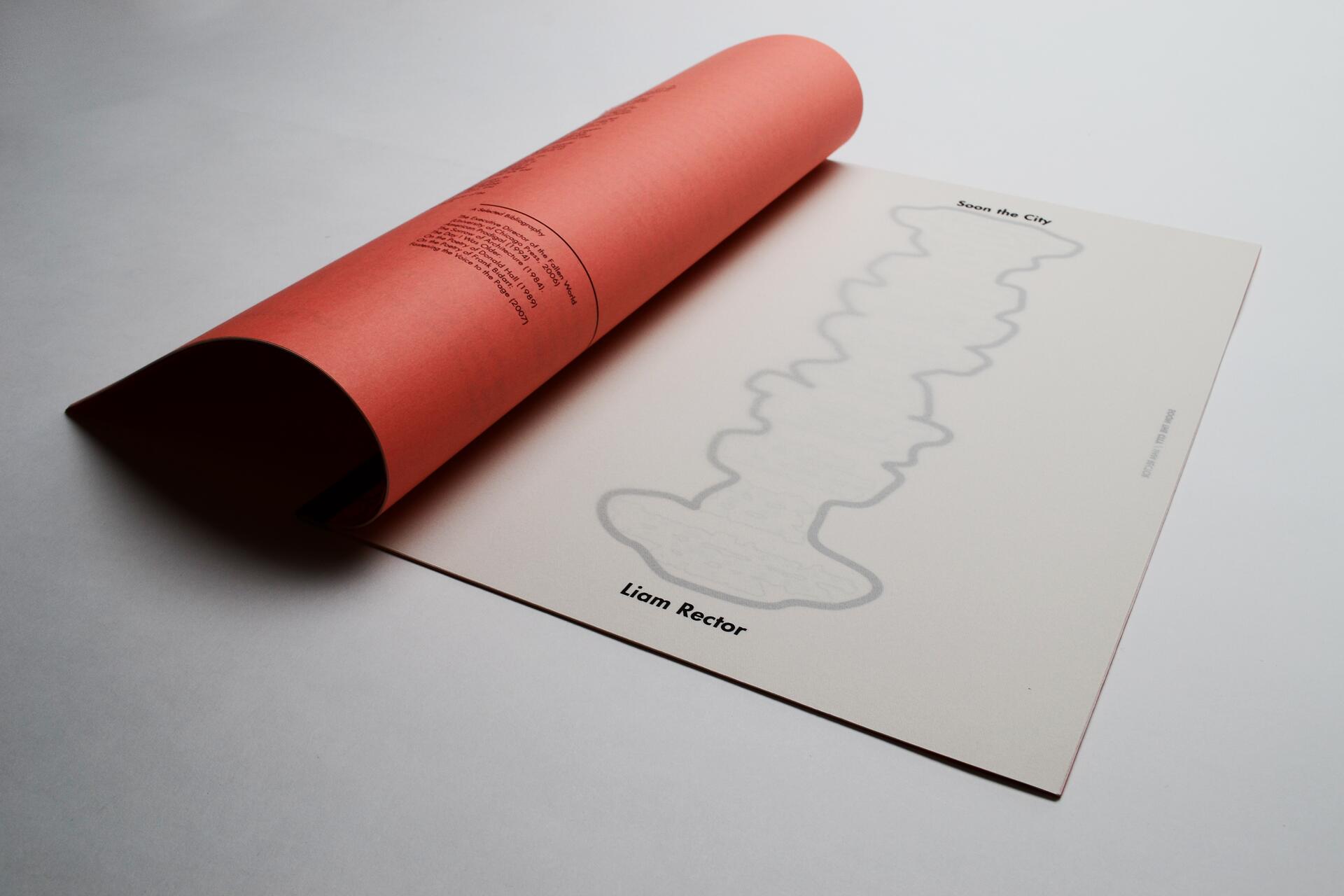 A page from a book partially rolled over, with a red cover and a grey outline of an abstract shape on a white page. The names "Soon the City" and "Liam Rector" are visible.