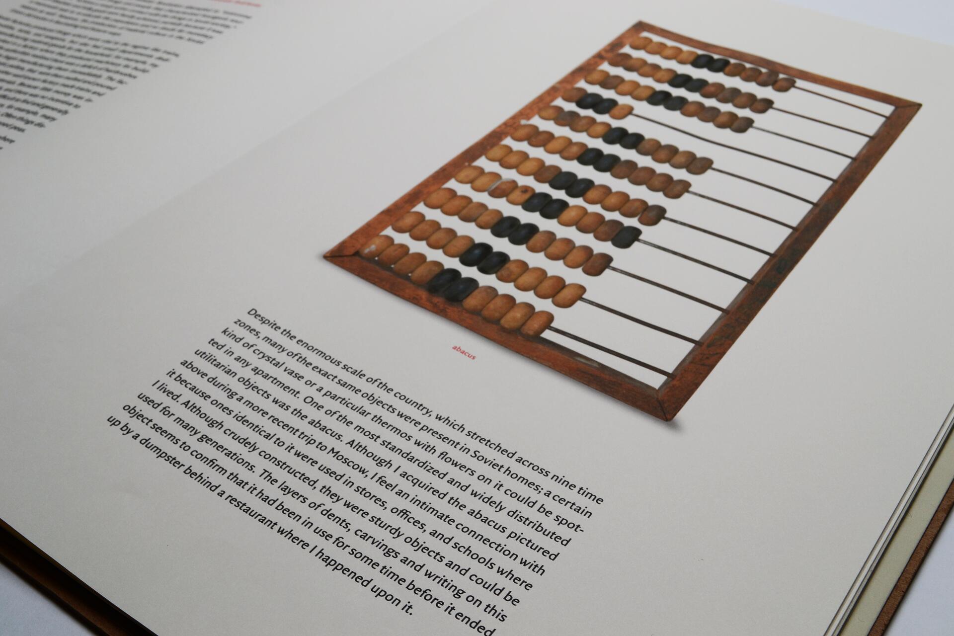 An open book displaying a photograph of a wooden abacus with brown and black beads. The abacus is positioned on the right page, while text is visible on the left and center.