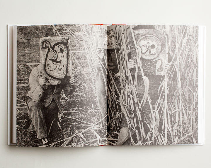 Two people wearing abstract face masks hide among tall grass, depicted in a black and white photograph within an open book.