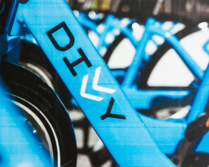 Close-up of a blue bike with "DIVVY" printed on the frame in black and white letters. Multiple similar bikes are blurred in the background.