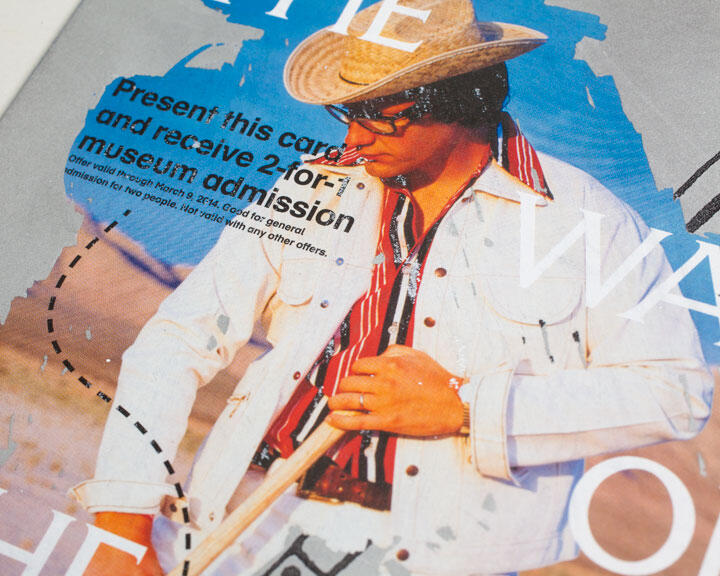 Man in a cowboy hat and sunglasses wearing a white jacket and red-striped shirt.