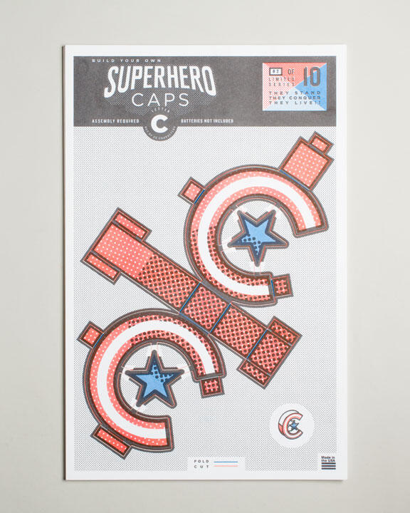 Decorative comic-style sheet with cut-out superhero symbols, featuring red and white stripes, blue stars, and text "Superhero Caps." Includes instructions for assembly.