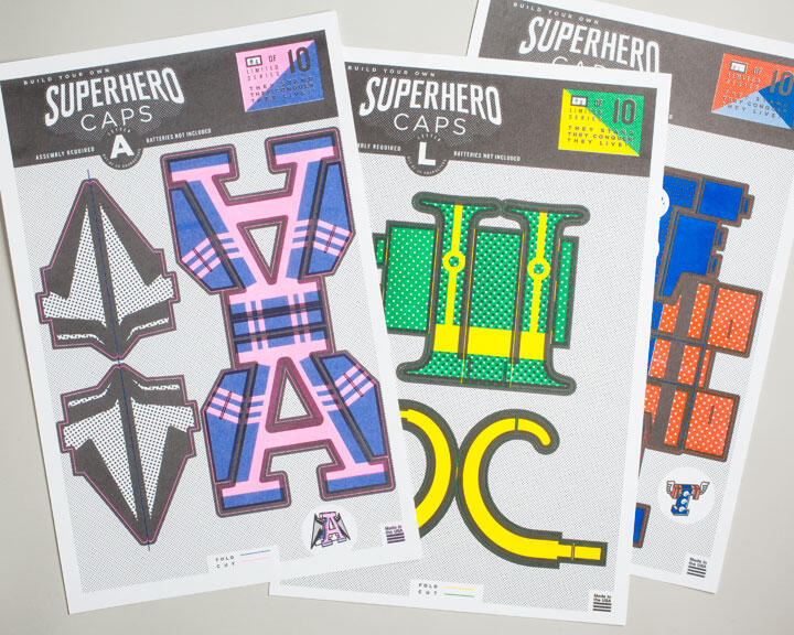 Three sheets for assembling superhero caps, each with colorful cut-out patterns and labeled parts. The visible sheets feature different designs in plaid pink, green with dots, and bold colors with letters. Text on top indicates they are superhero caps.