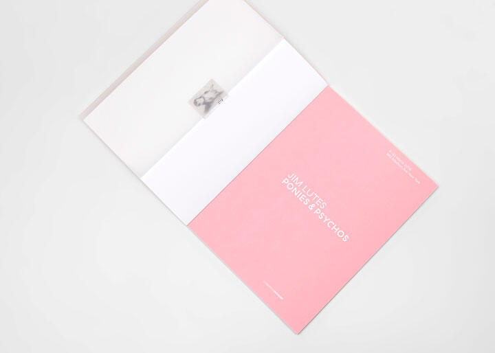 Open book with a pink page on the right, featuring white text. A small photo is partially visible on the left white page. The background is light gray.