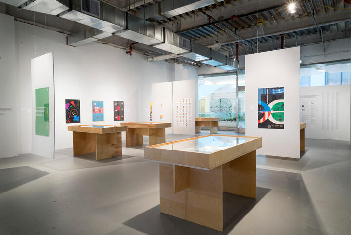 Modern art gallery interior with wooden display tables and wall art exhibits. Bright lighting accents posters and architectural elements.