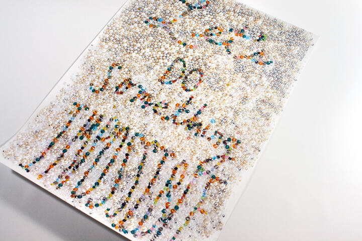 A sheet covered with numerous small, colorful beads forming patterns and text, set against a white background.