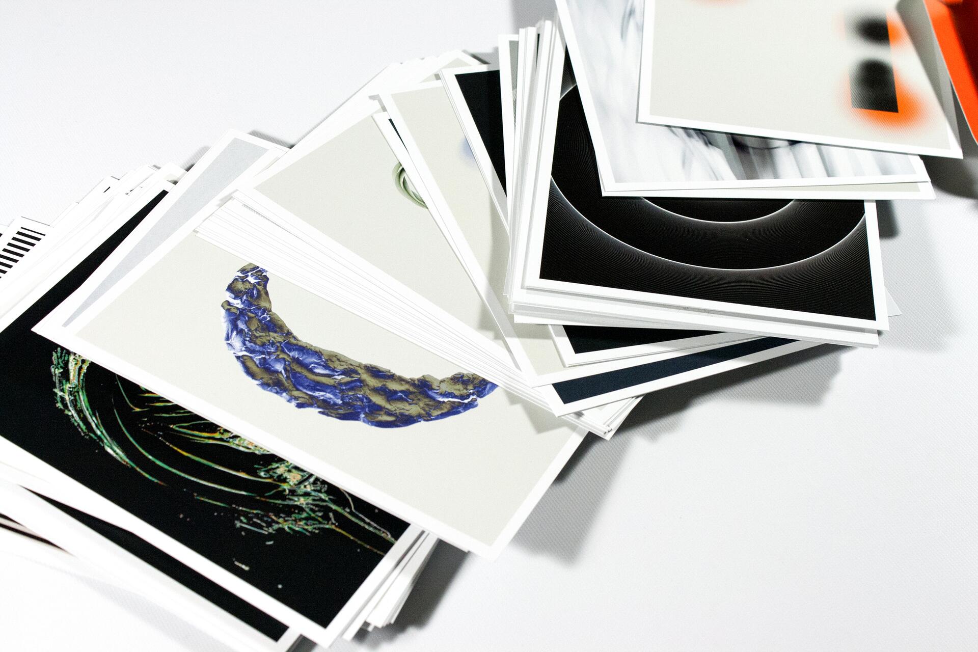 A stack of abstract art prints featuring various designs and colors, including a blue crescent shape and black circular patterns.