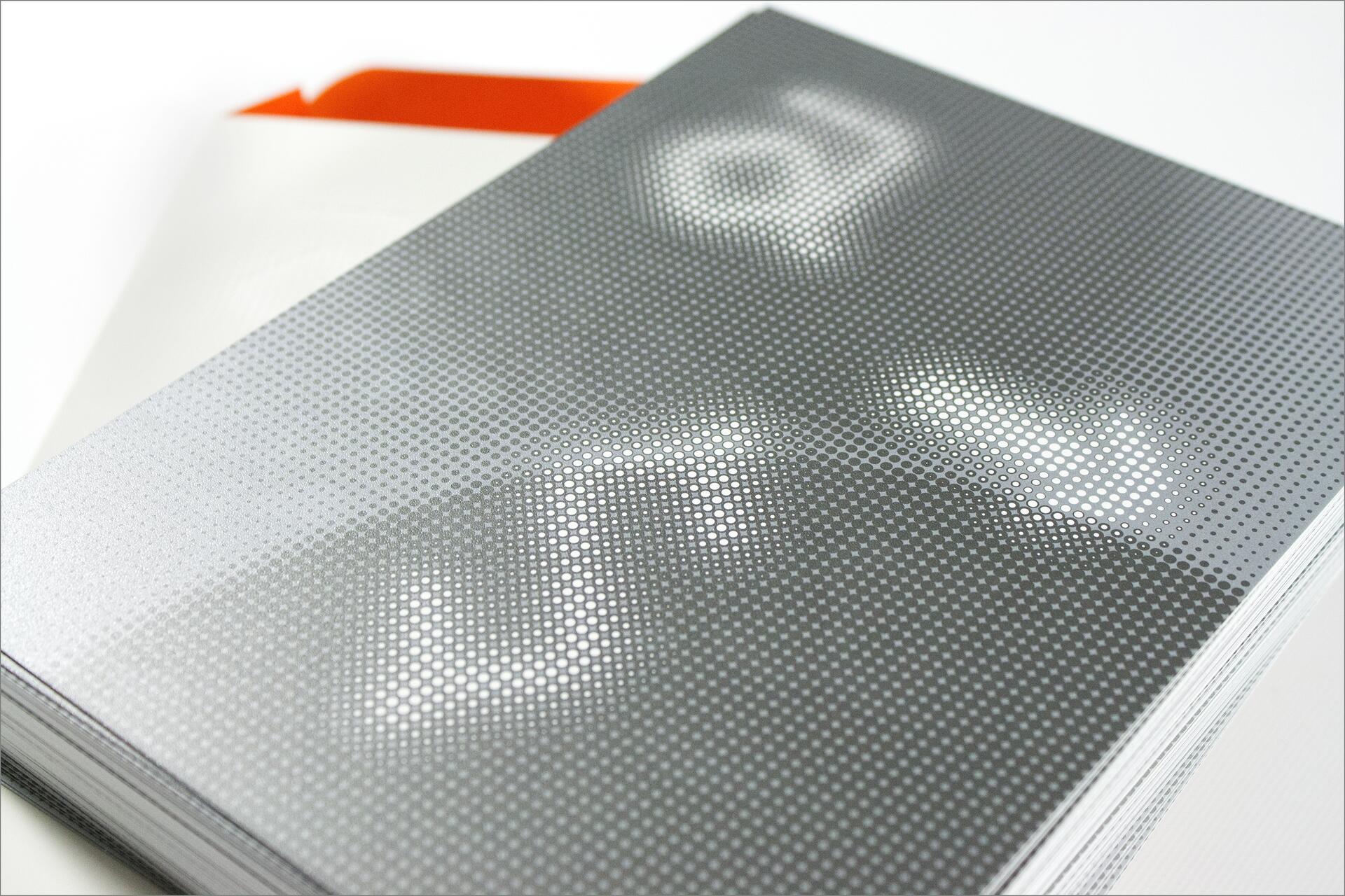 Close-up of a stack of glossy brochures with a pixelated pattern and abstract design in white and gray, featuring prominent dot textures.