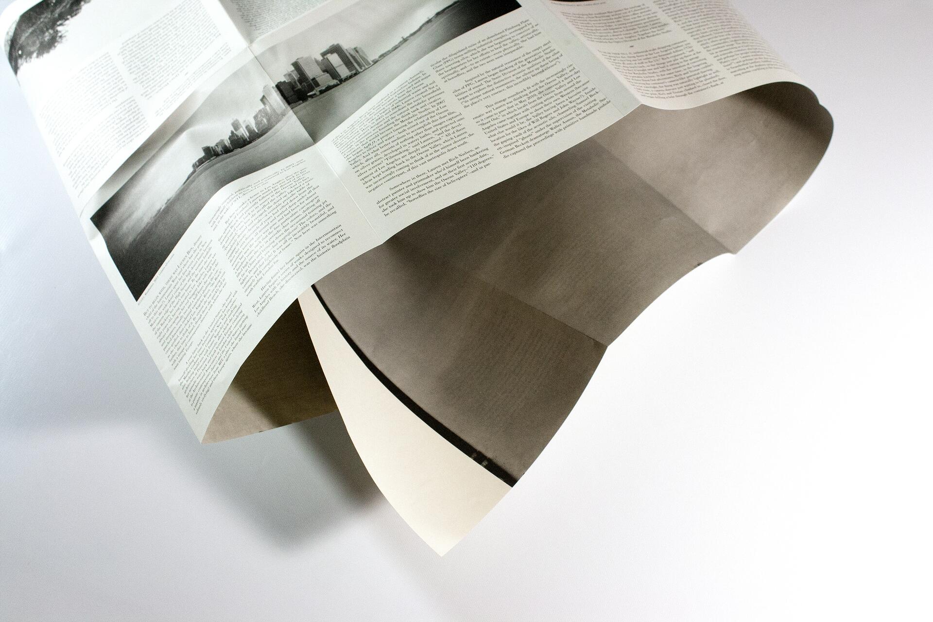 Open newspaper with black and white cityscape photo, floating in the air against a white background.
