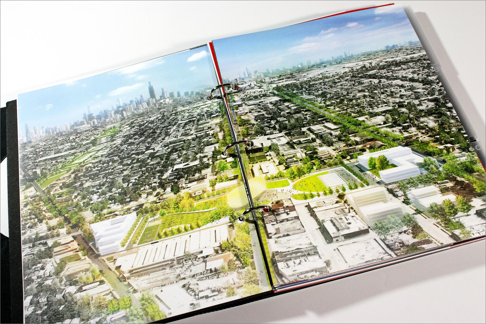 Open binder displaying an aerial photograph of a cityscape, featuring densely packed buildings with a park and greenery in the foreground. A city skyline is visible in the distance under a clear blue sky.