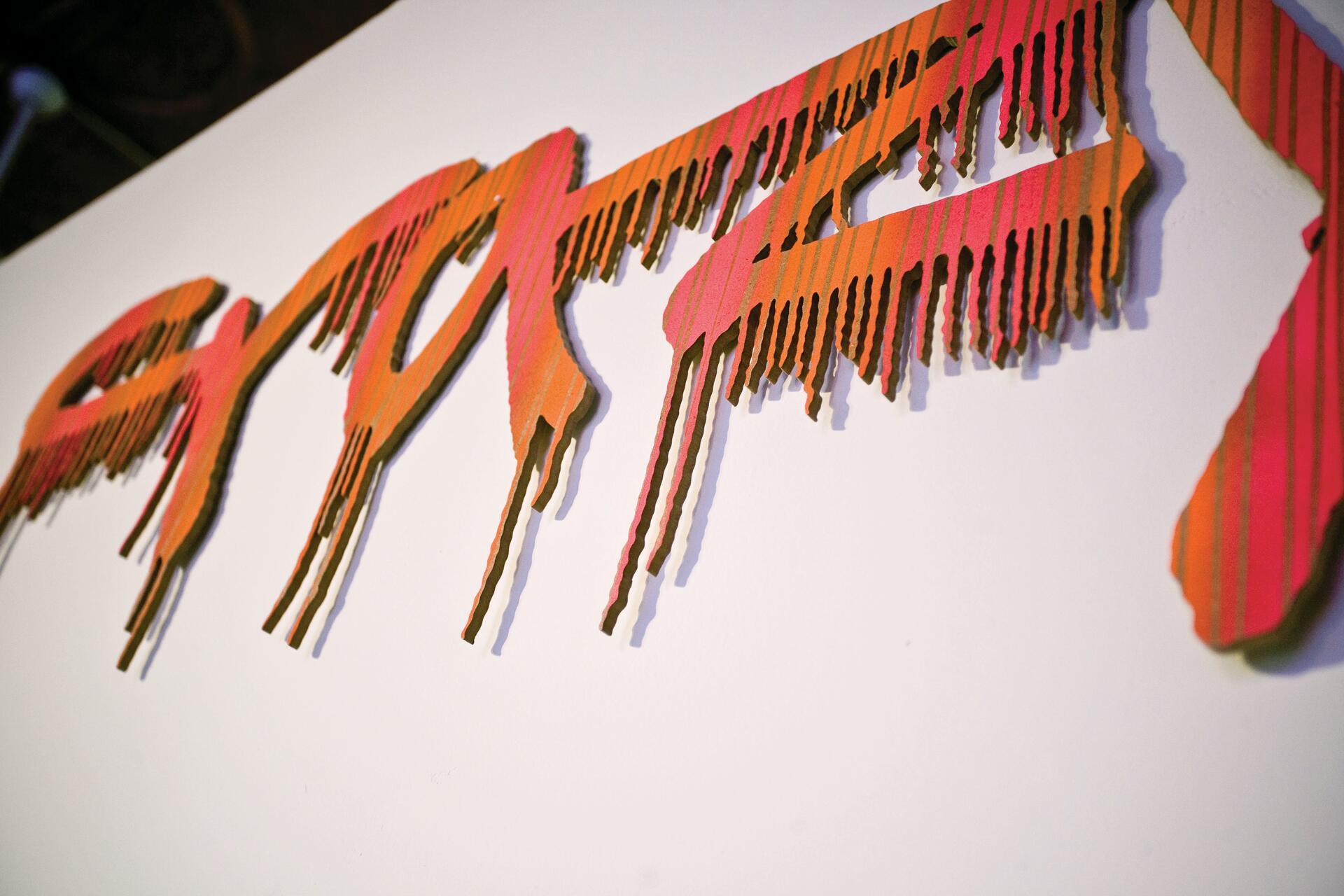 Red and orange abstract cardboard cutouts resembling dripping paint on a white background, casting shadows.