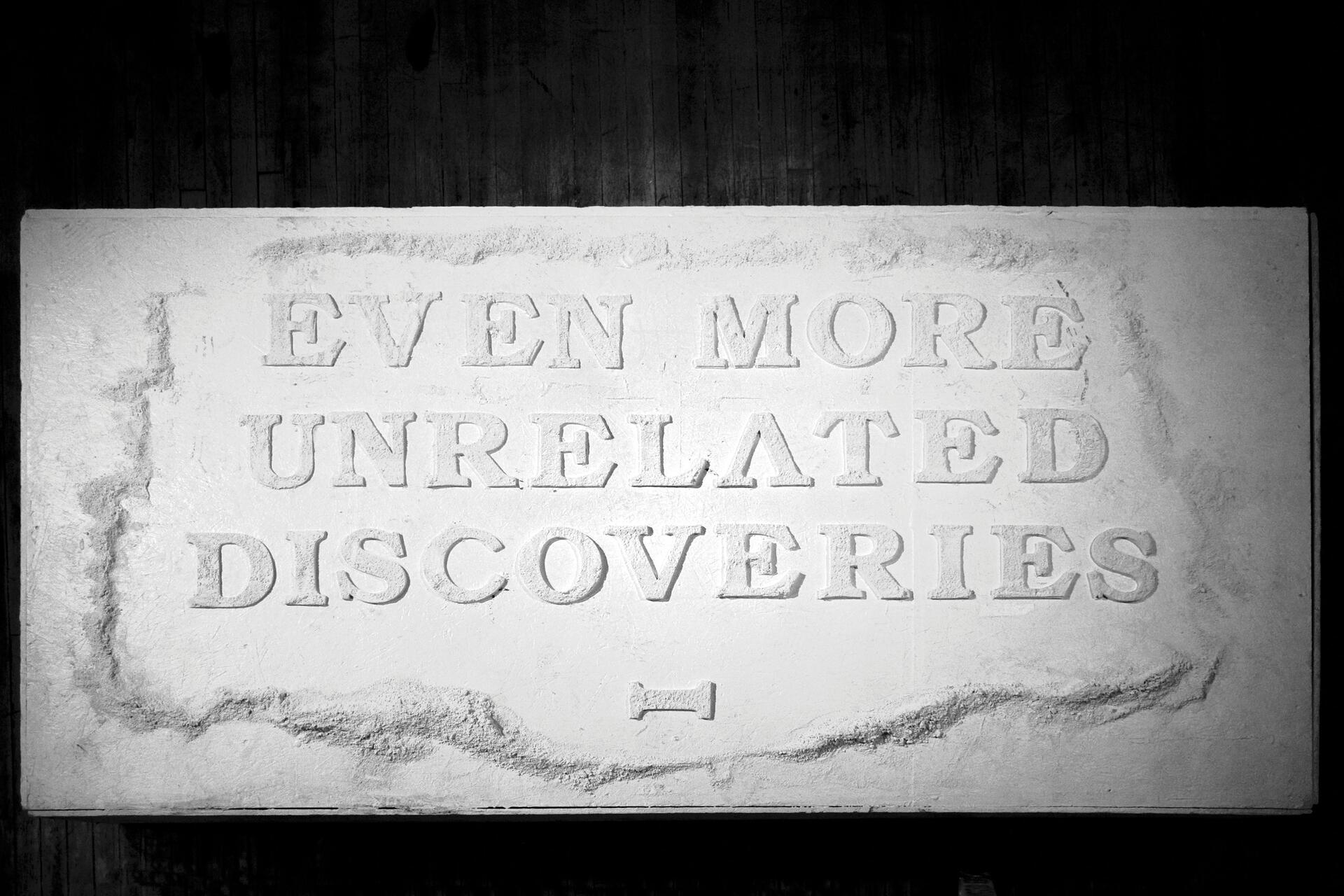 Stone slab with carved text reading, "Even More Unrelated Discoveries," in capital letters. The surface appears textured and slightly weathered, with shadows accentuating the letters.