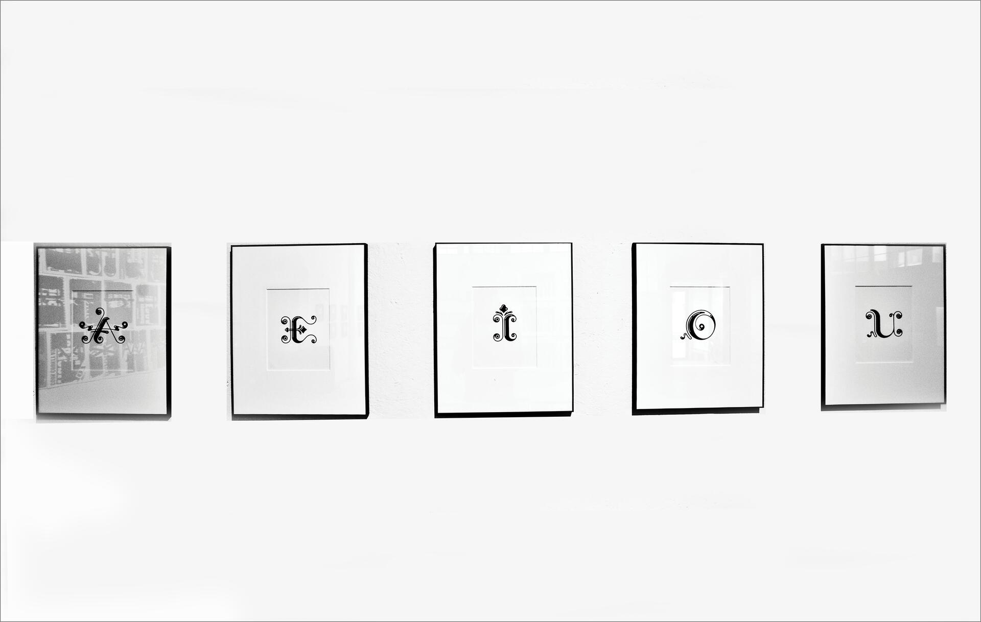 Five framed calligraphic symbols in a row against a white wall, each with a unique, ornate design.
