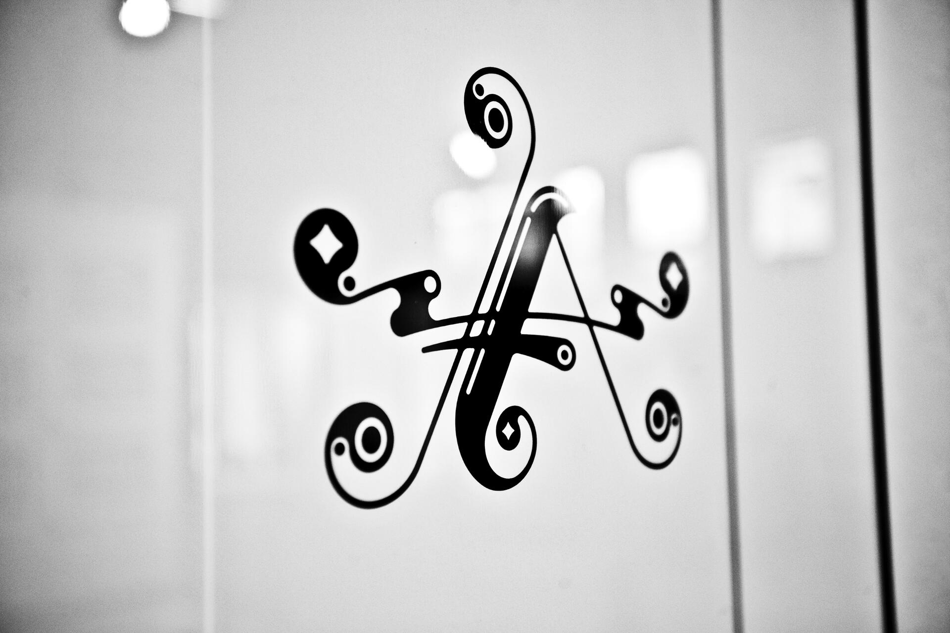 Black ornate letter "A" design on a frosted glass surface in grayscale.