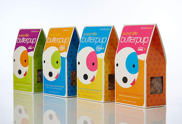Colorful cardboard packages of dog treats with a playful dog face design, arranged in a row. Each box is a different color: green, blue, orange, and pink, with star patterns and labeled "sweet little butterpup."