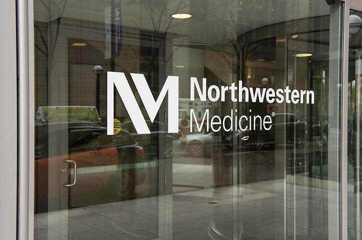 Northwestern Medicine logo on a glass door with a city street reflected in the background.
