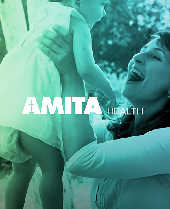A woman joyfully lifts a baby in an outdoor setting with a greenish tint. The AMITA Health logo is prominently displayed in the foreground.