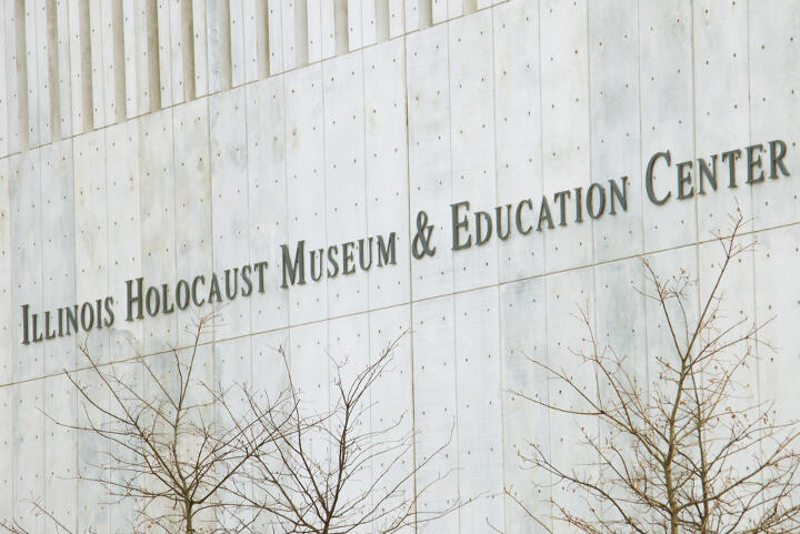 Illinois Holocaust Museum & Education Center sign on a concrete wall with leafless trees in the foreground.