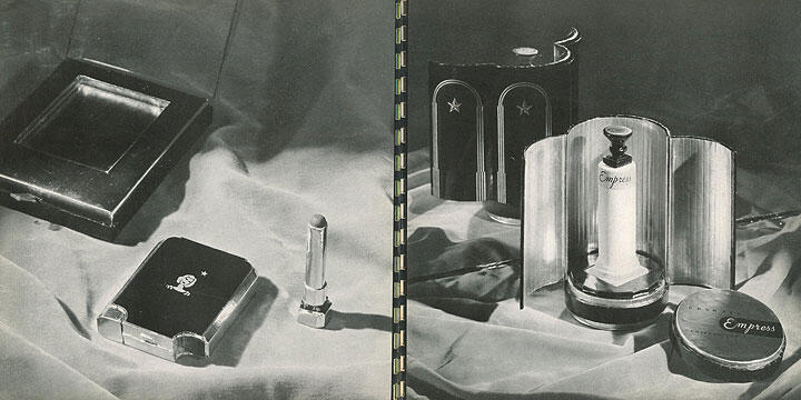 Vintage black and white photograph of elegant cosmetic products on a silky fabric. On the left, a compact and lipstick. On the right, a perfume bottle labeled "Empress" with an open metallic case and a round powder container.
