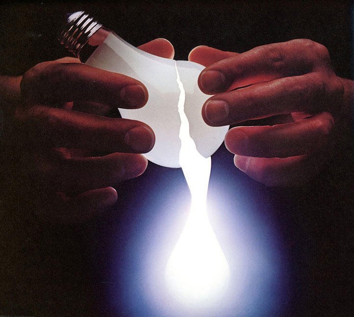 Hands tearing a light bulb in half, emitting a bright white glow against a dark background.