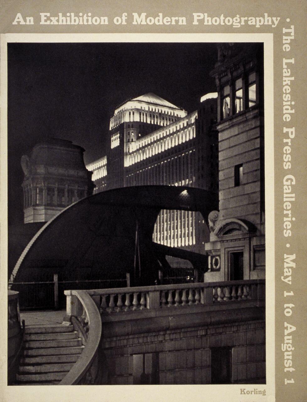 Black and white photograph of a cityscape at night, featuring illuminated architectural buildings with a curved staircase and ornate detailing in the foreground.