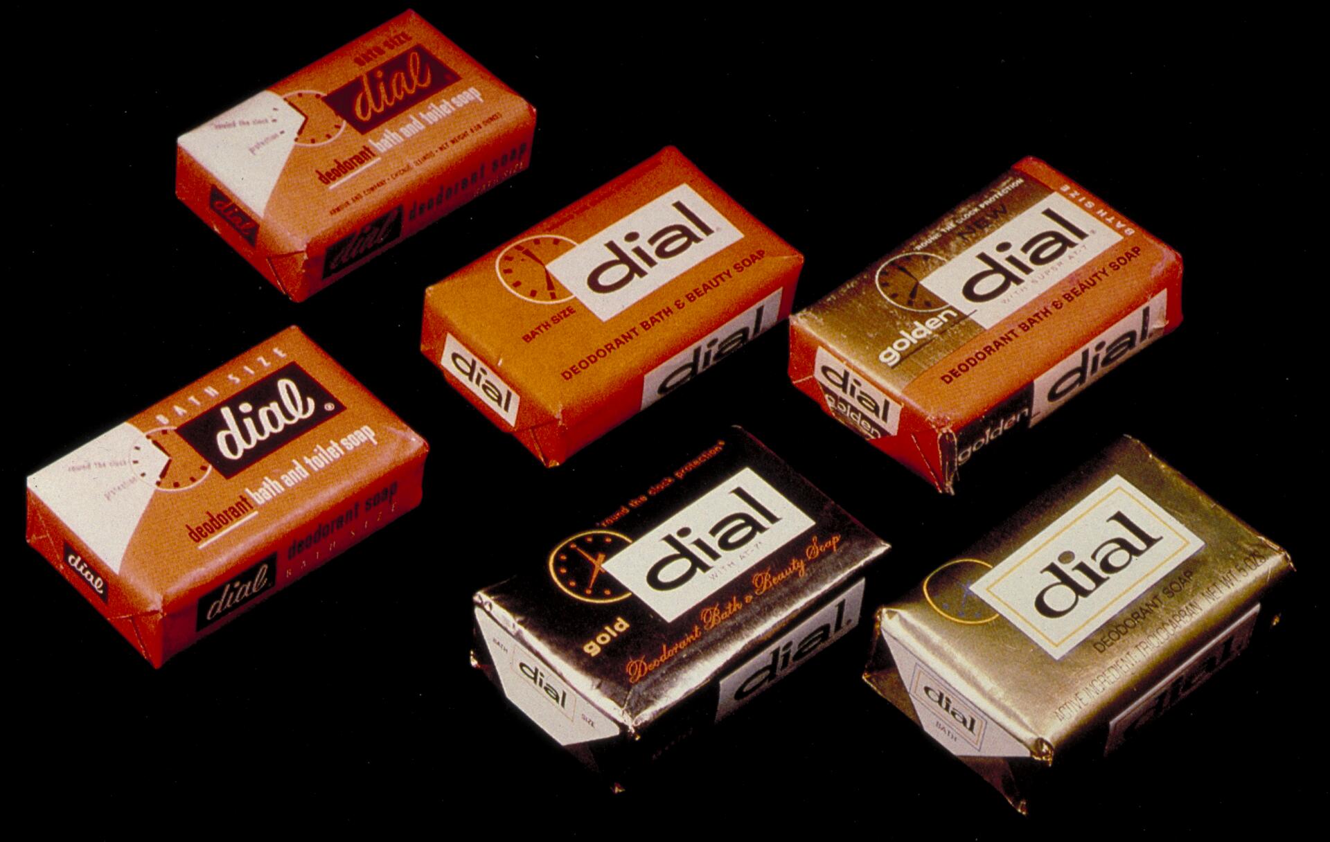 Six bars of Dial soap in various orange and gold packaging on a black background.