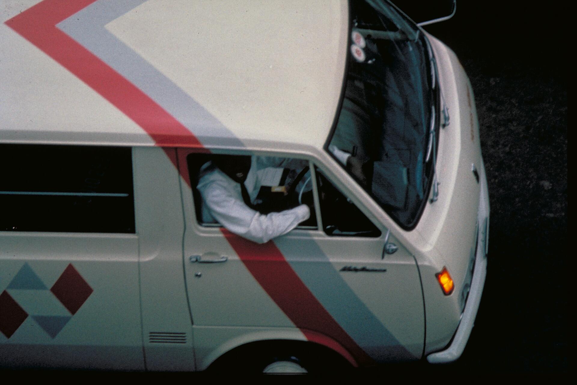 White van with red geometric design, view from above, driver in white shirt, driving on a dark road.