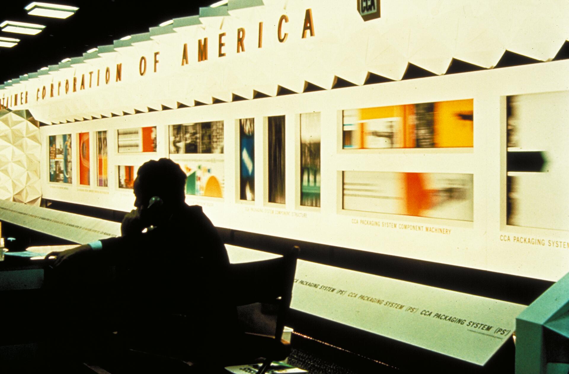Exhibition display with illuminated images on a wall, silhouetted person on a phone in the foreground.