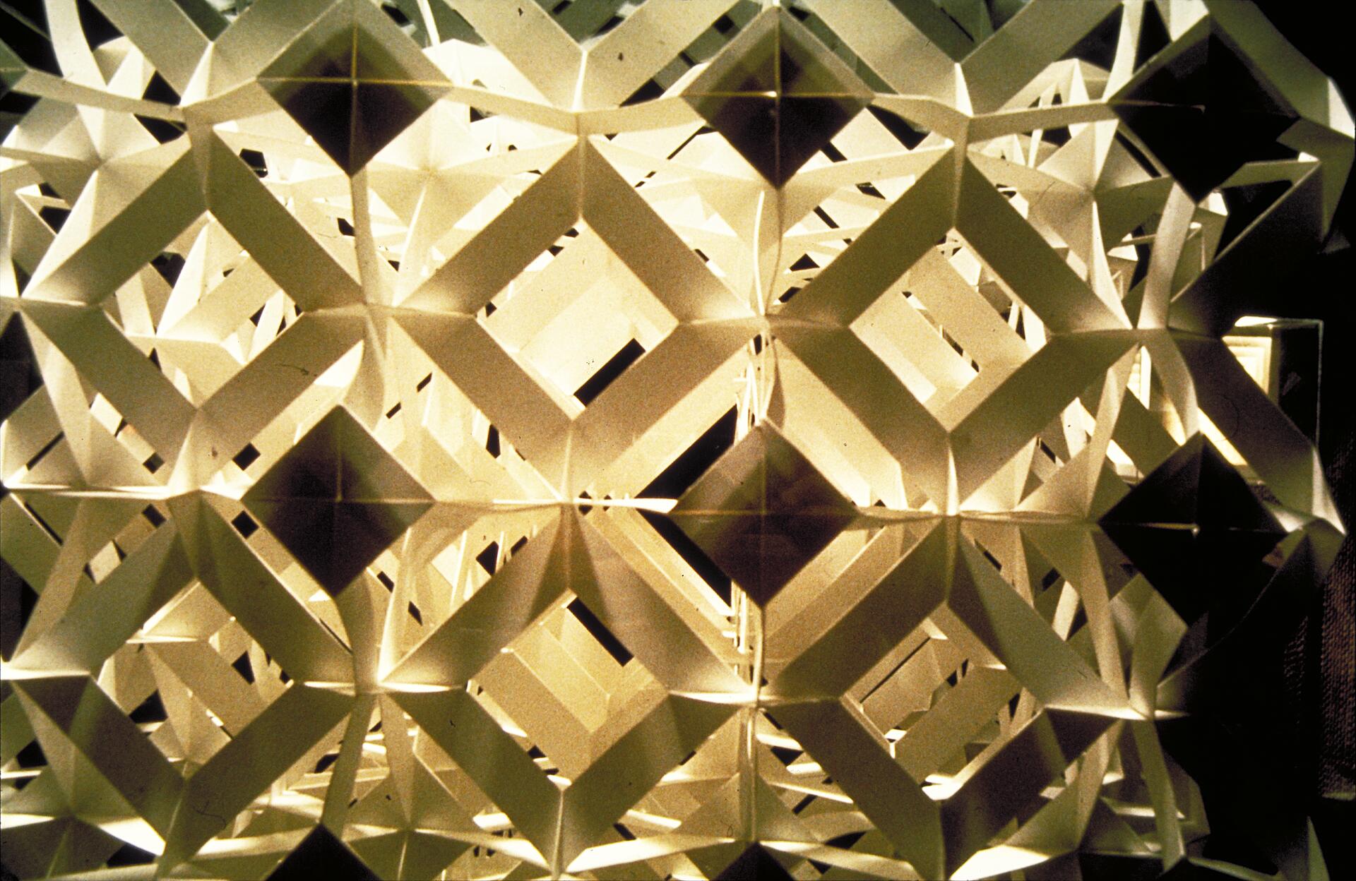 Geometric paper sculpture with interlocking diamond shapes, illuminated from behind, creating intricate patterns and shadows.