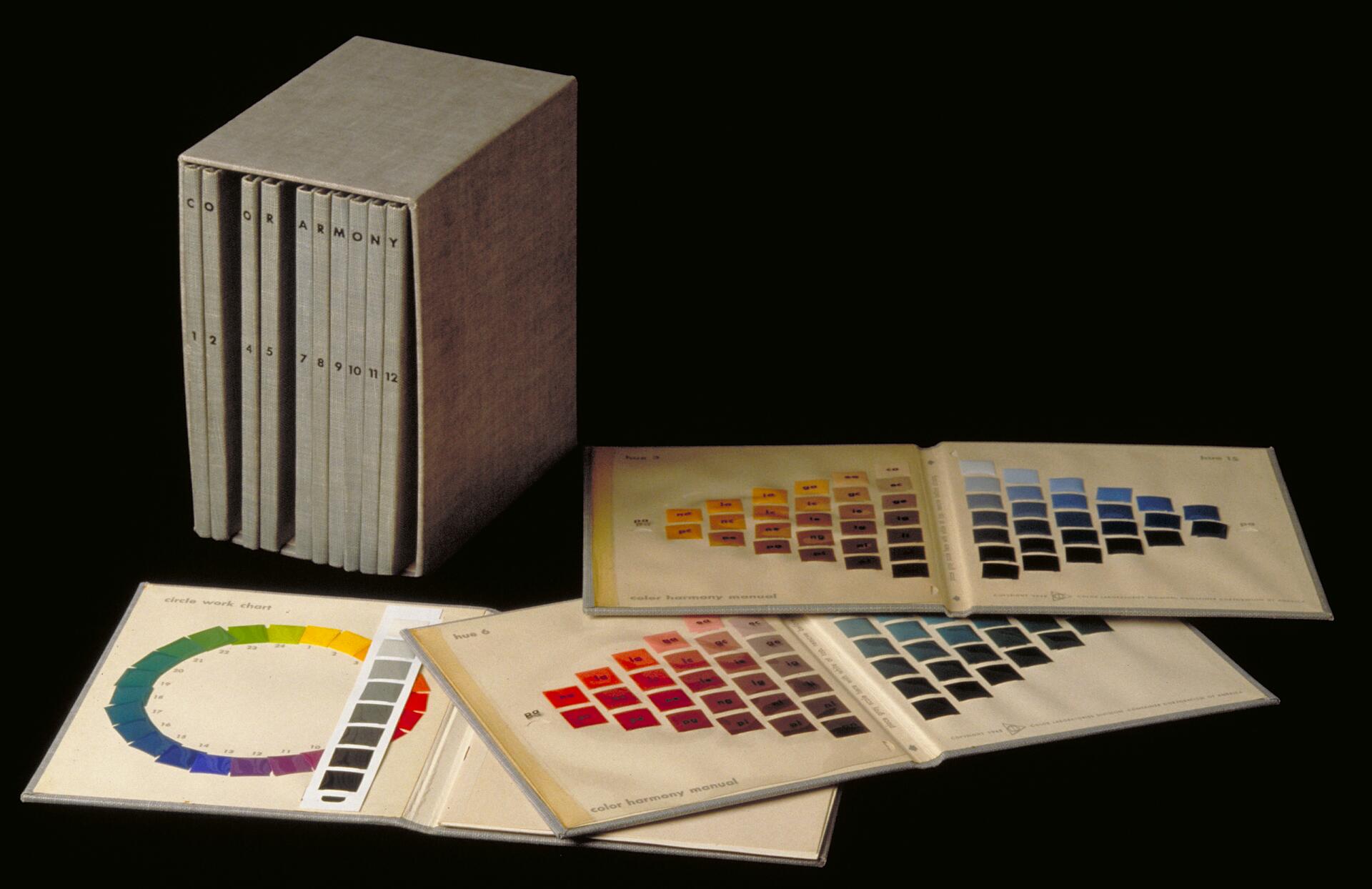 Box set titled "Color Harmony" with 12 volumes, displayed alongside open manuals showing color swatches in various hues, arranged in grids.