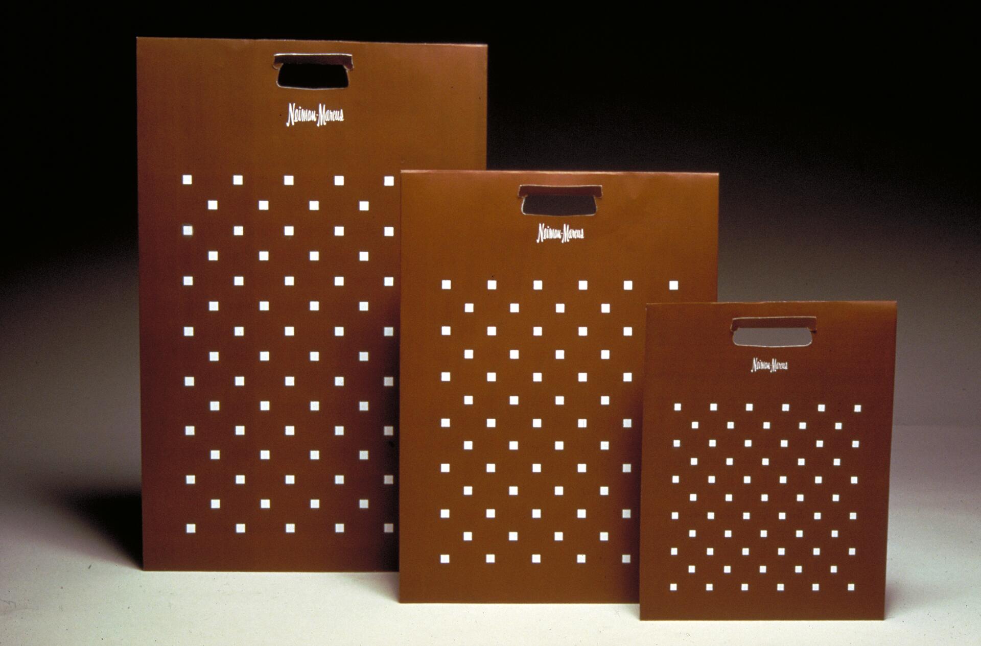 Three brown Neiman Marcus shopping bags with white square patterns, arranged from largest to smallest.