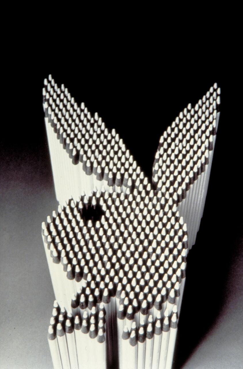 Pencils arranged to form a 3D outline of a rabbit’s head with ears, viewed from above on a dark background.