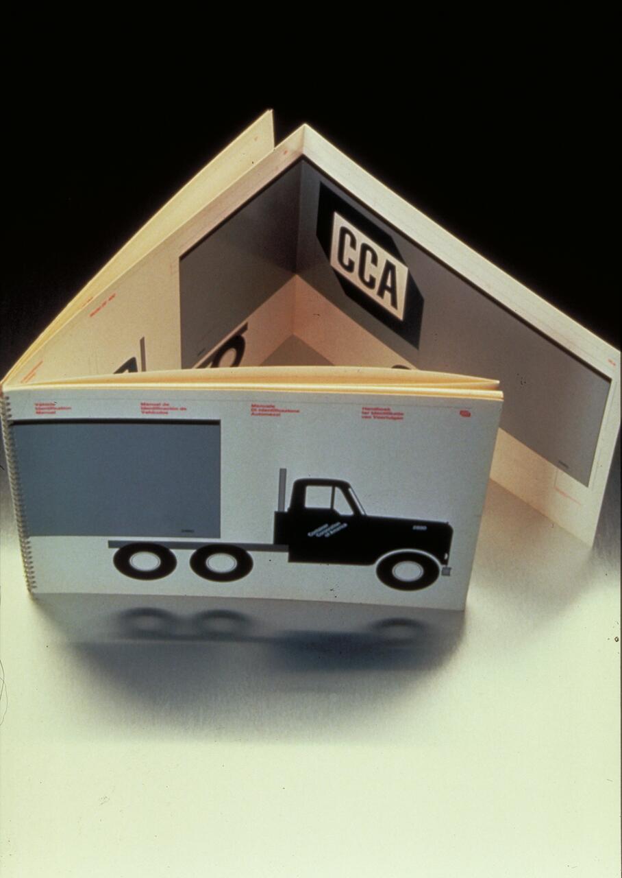 Two open pages of a book featuring a stylized black and gray truck graphic, and a "CCA" logo on the inner page. The background is neutral, enhancing the design.
