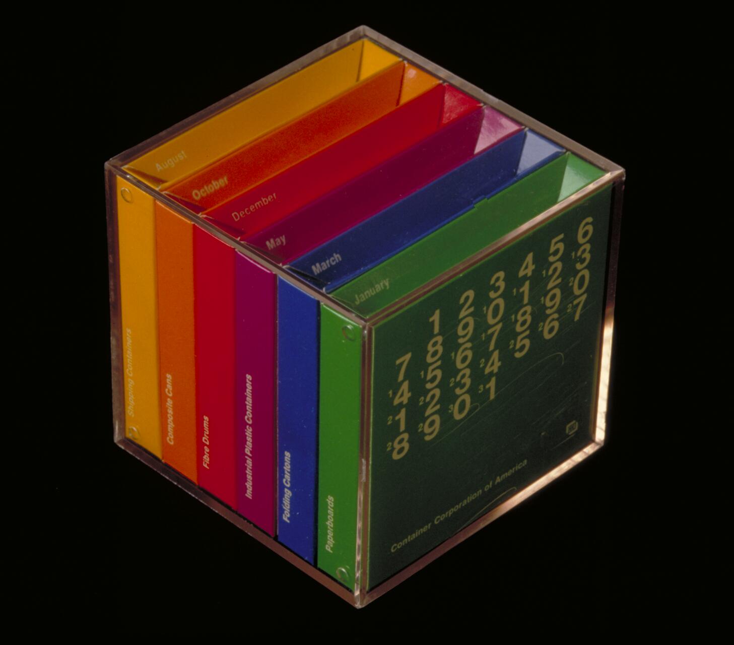 Colorful cubical calendar with rotating cards for months and days, encased in clear plastic. Each card has a month name and a related topic in white text, visible are August, October, December, May, March, and January.