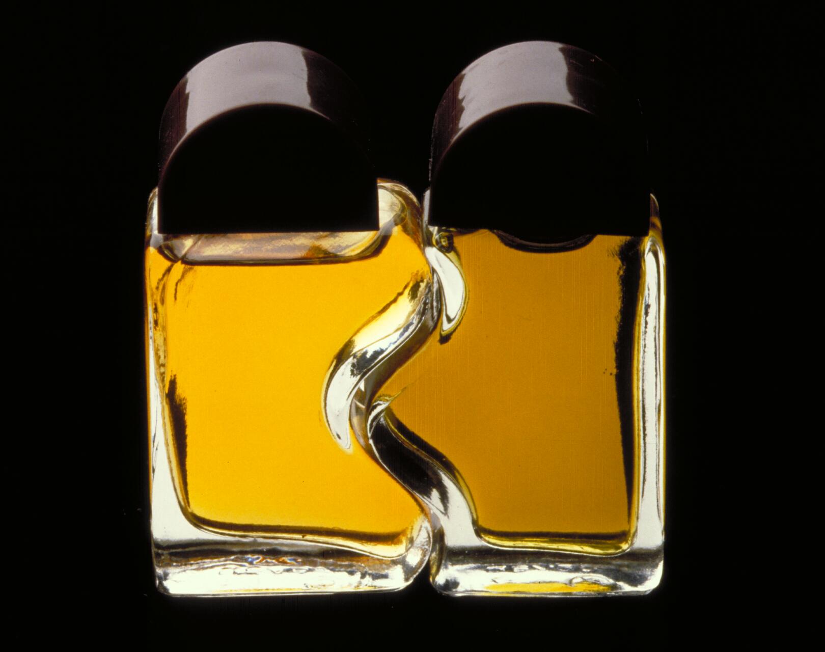 Two interlocking perfume bottles with dark caps, filled with amber liquid, against a black background.